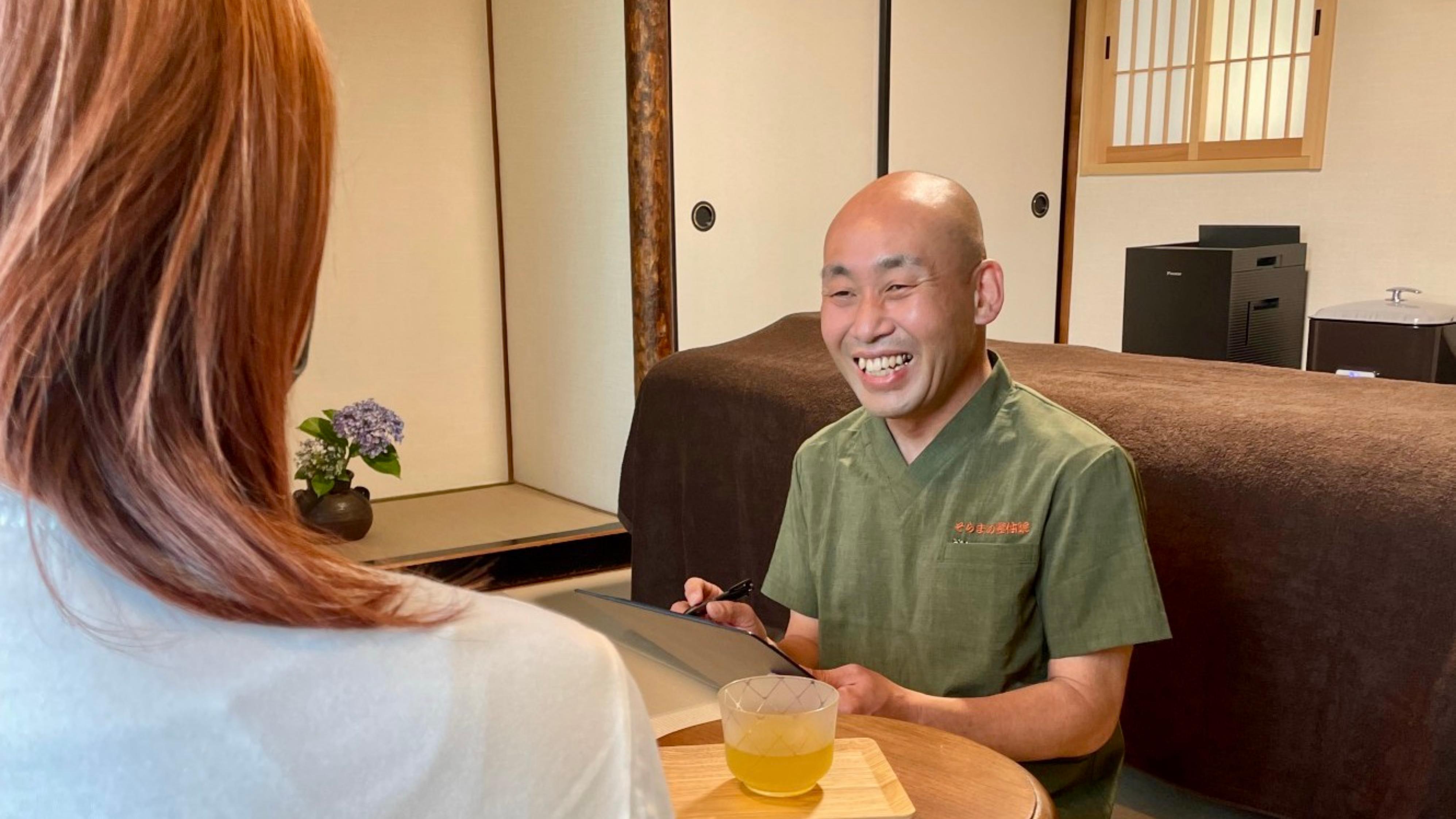 Smiling Japanese Reiki practitioner consulting with a guest in a private tatami room, offering tea before the session in Takarazuka, Japan